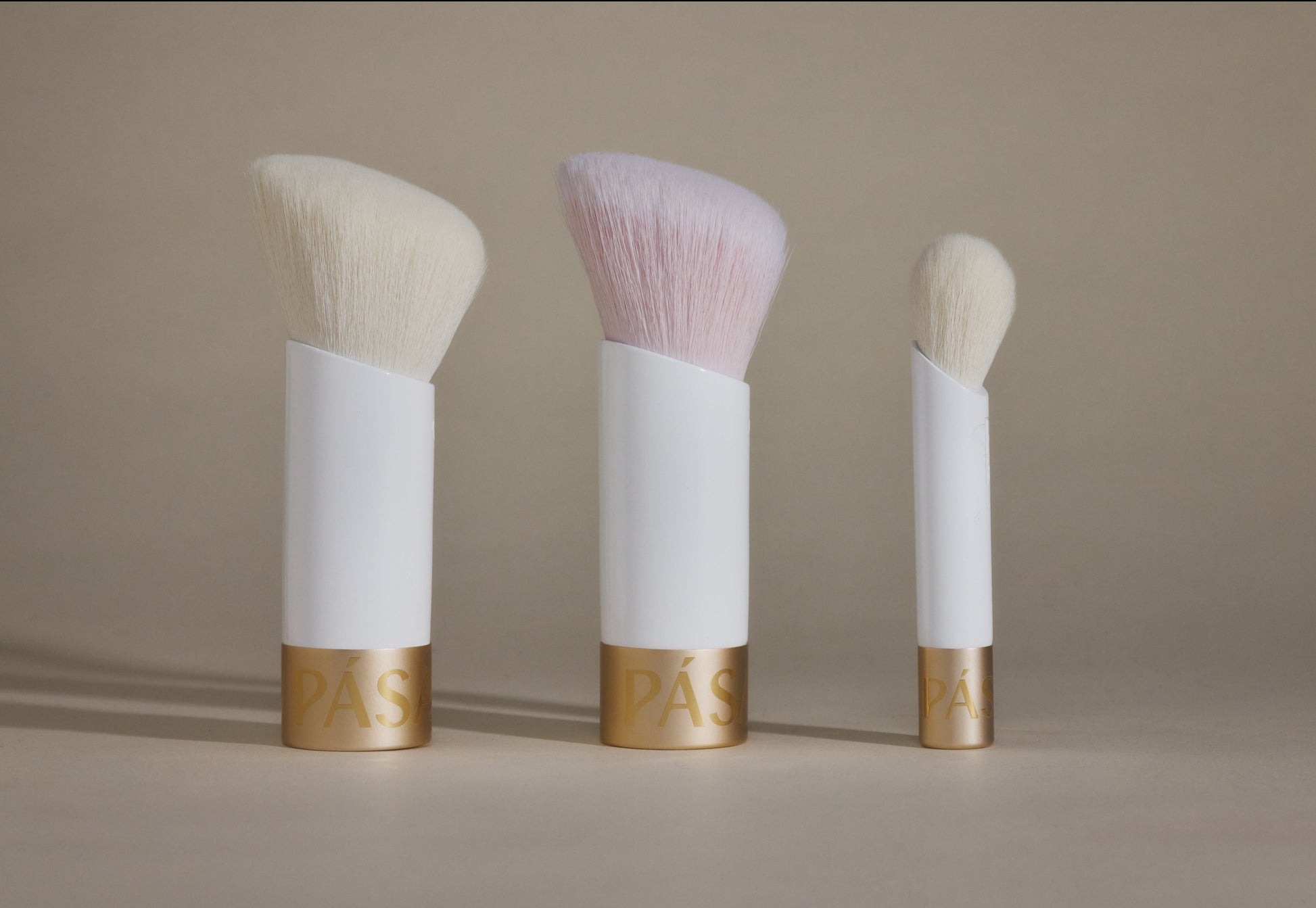 Three makeup brushes standing up and aligned straight across on taupe background